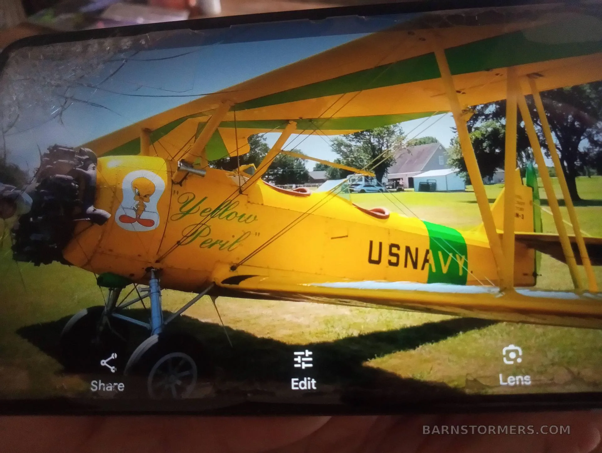 A photo of a yellow and green N3N biplane, labeled "US NAVY" and "Yellow Peril" with a Tweety Bird cartoon, is displayed on a phone screen.