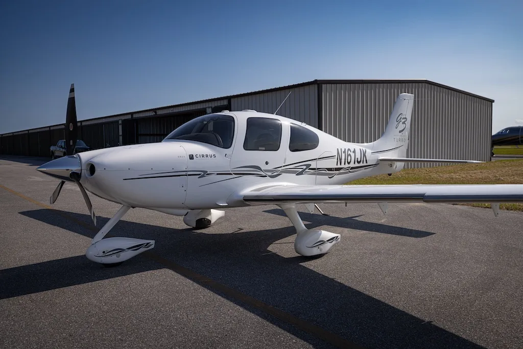 A white Cirrus SR22 G3 Turbo aircraft, registration N161JK, parked on an asphalt tarmac with a hangar in the background.