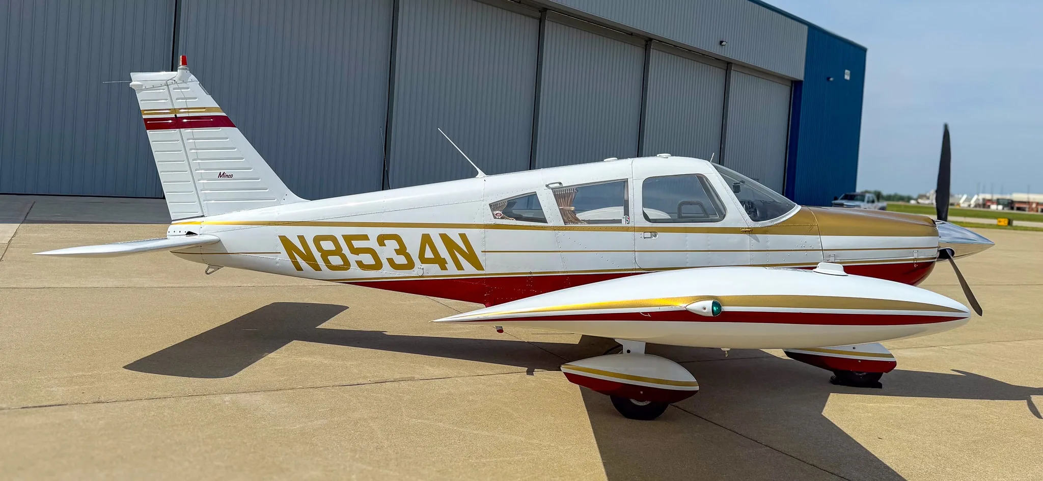 A side view of the white, red, and gold Piper Cherokee aircraft (N8534N) parked on an airfield.