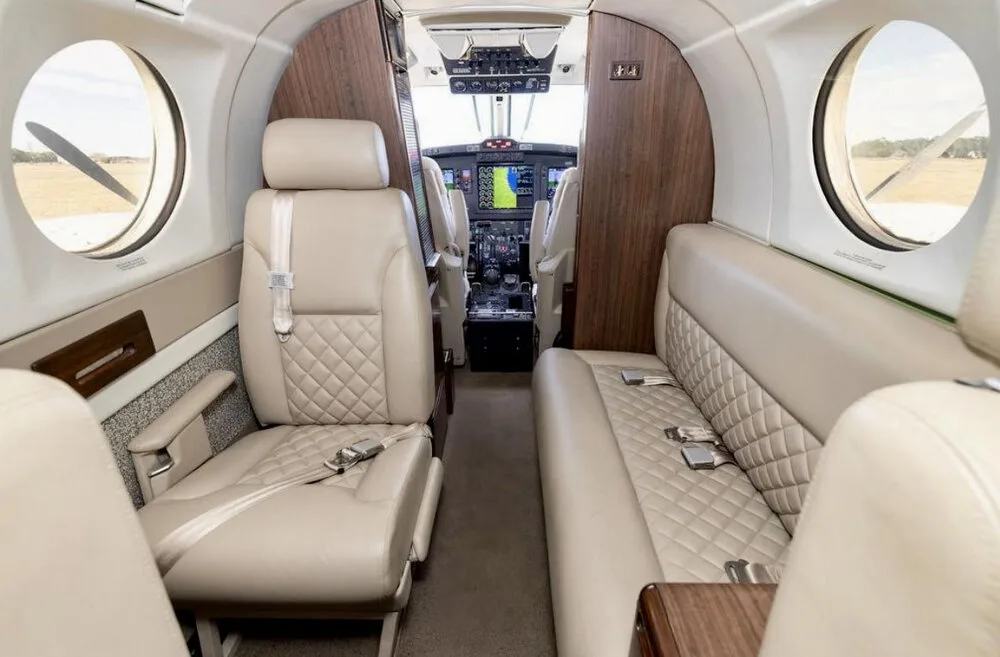 The aircraft cabin interior with beige quilted leather seats, looking forward into the cockpit.
