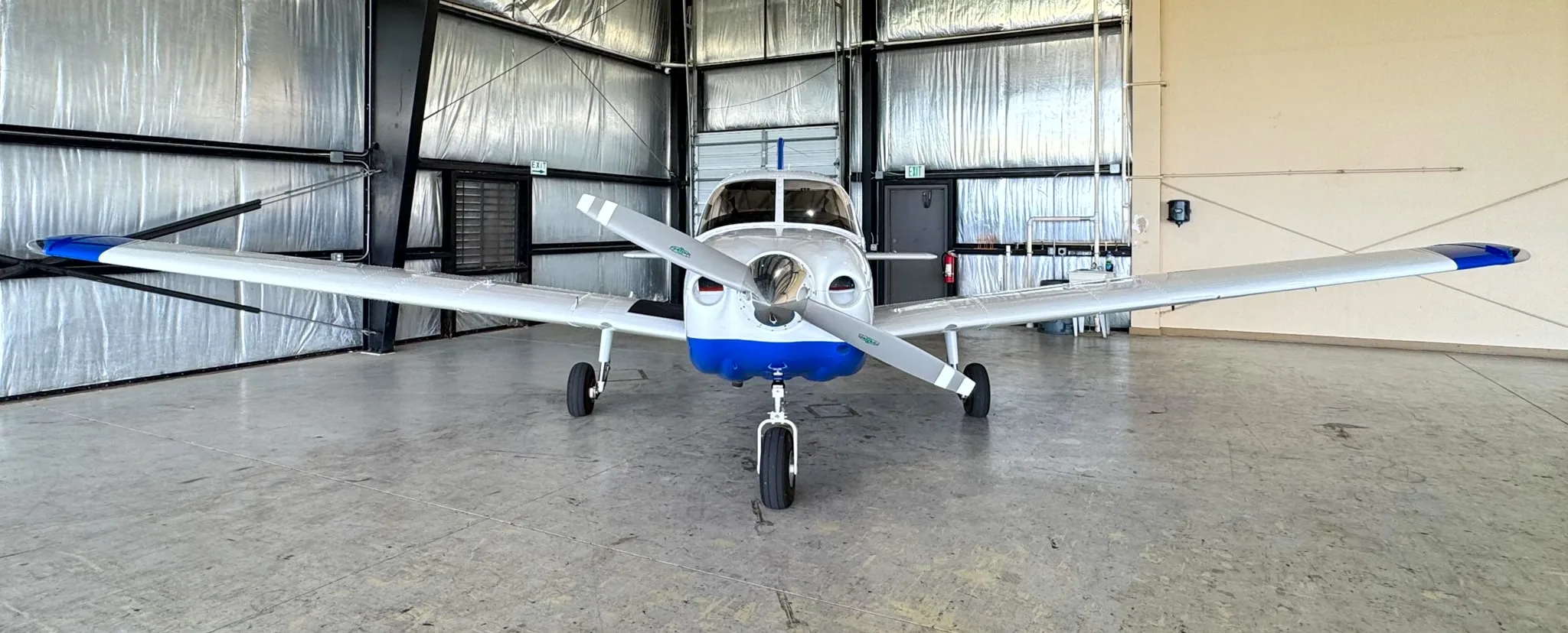 A head-on view of the white and blue Piper Archer TX aircraft, N105DJ, inside a hangar.
