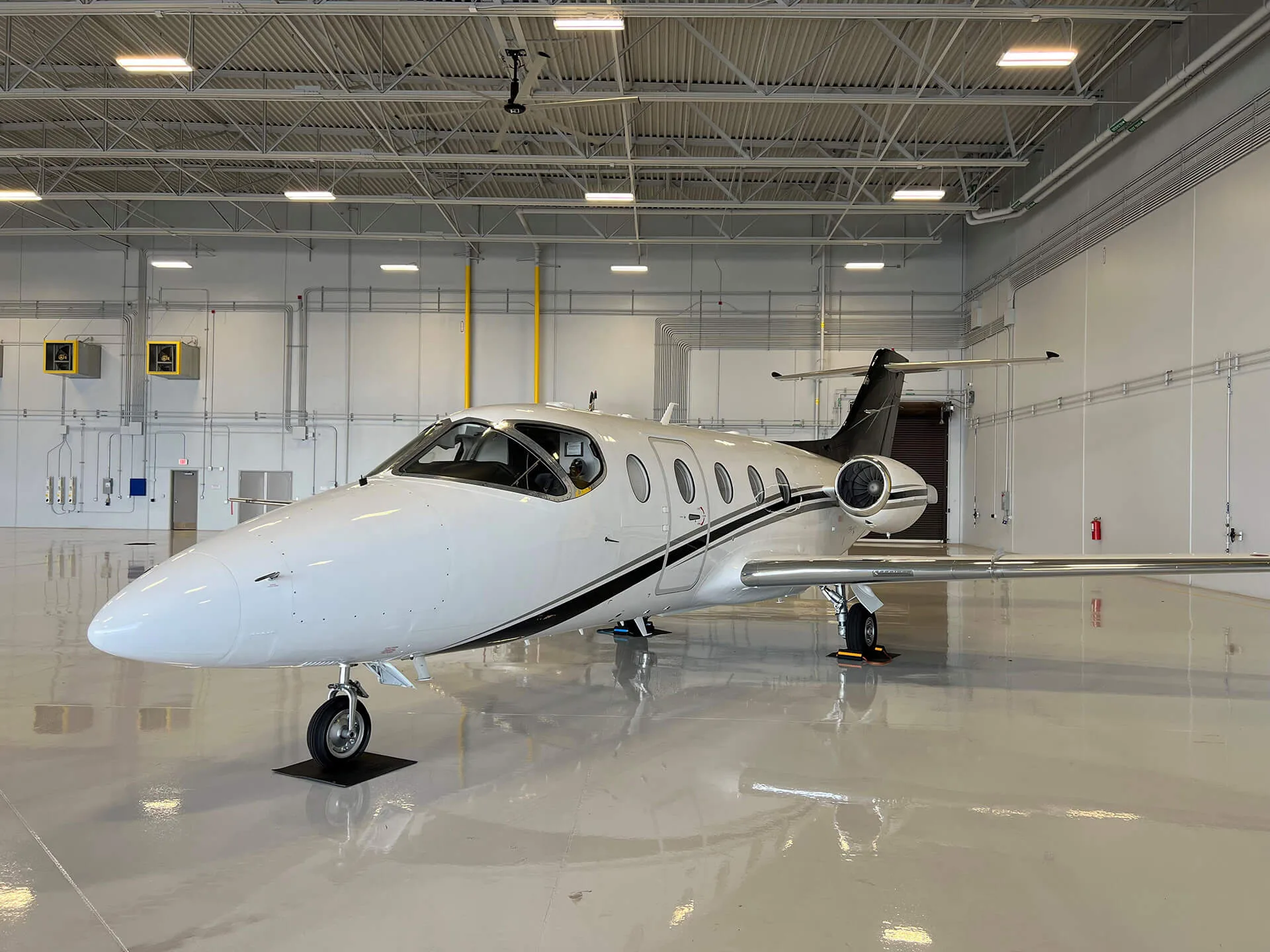 A white business jet with black stripes parked inside a brightly lit hangar.