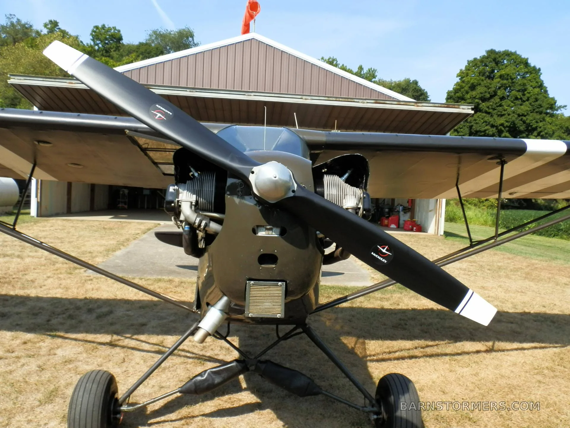 A front view of a black single-engine aircraft, showing its propeller, exposed engine, and landing gear.