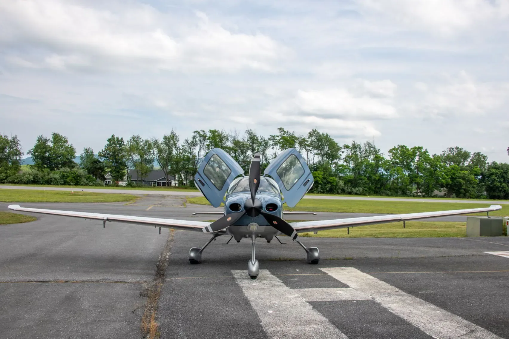 Front view of a blue Cirrus SR22T Carbon aircraft, N27MY, with its gull-wing doors open, on a runway.