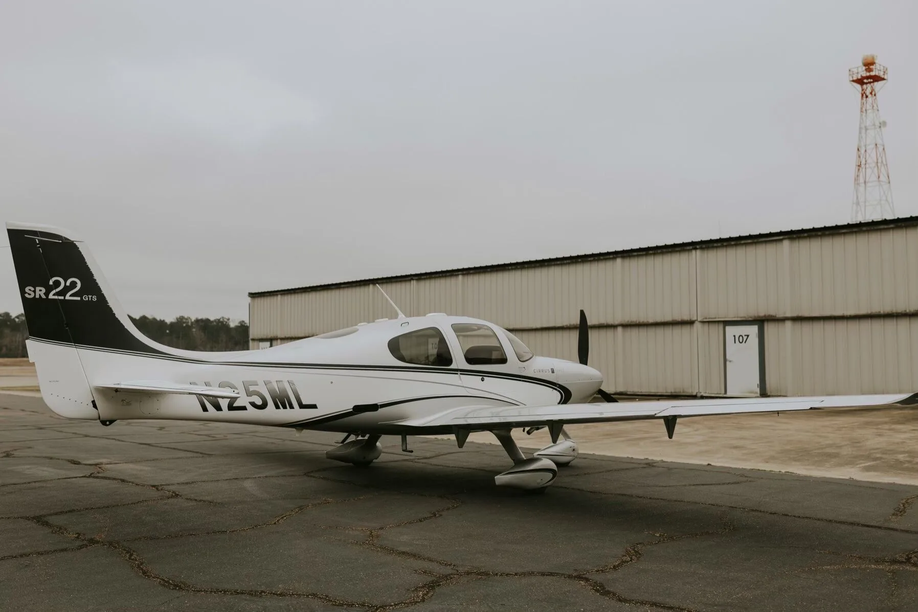 A three-quarter rear view of a silver Cirrus SR22 GTS aircraft with N25ML registration, parked on an asphalt ramp.