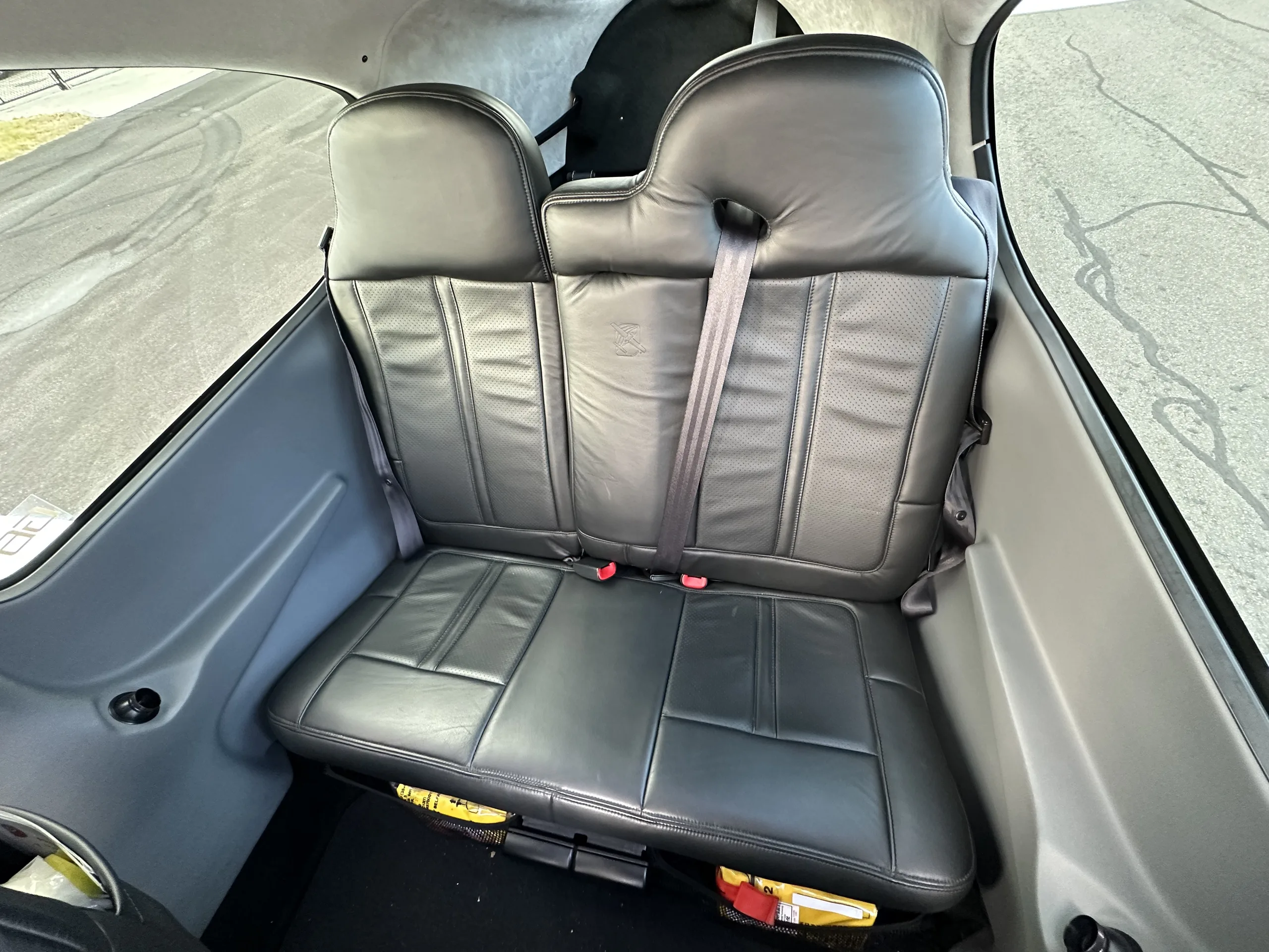 The rear two black leather seats of an aircraft cabin with seatbelts visible.