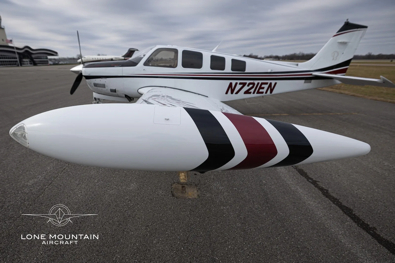 A close-up view of the right wingtip tank of the N721EN aircraft, showing its white, black, and red stripe paint scheme.