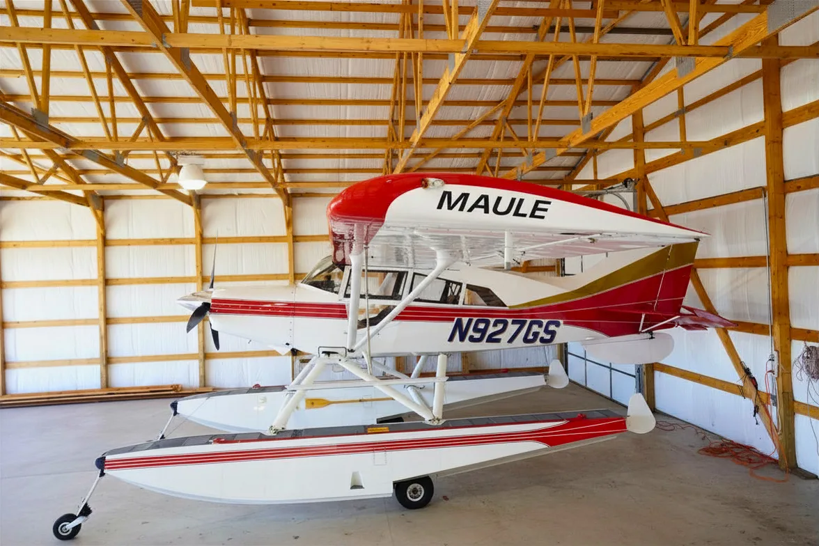 A red, white, and gold Maule floatplane with registration N927GS parked in a hangar.