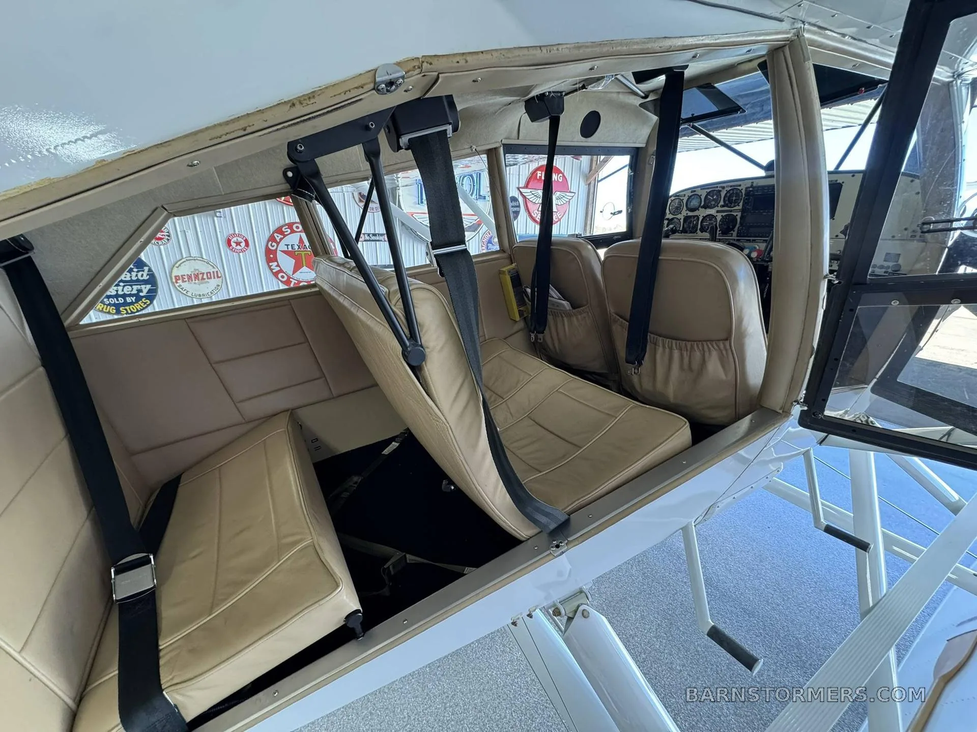 The tan interior cabin of a floatplane, showing two rows of seats with seatbelts, looking towards the cockpit.