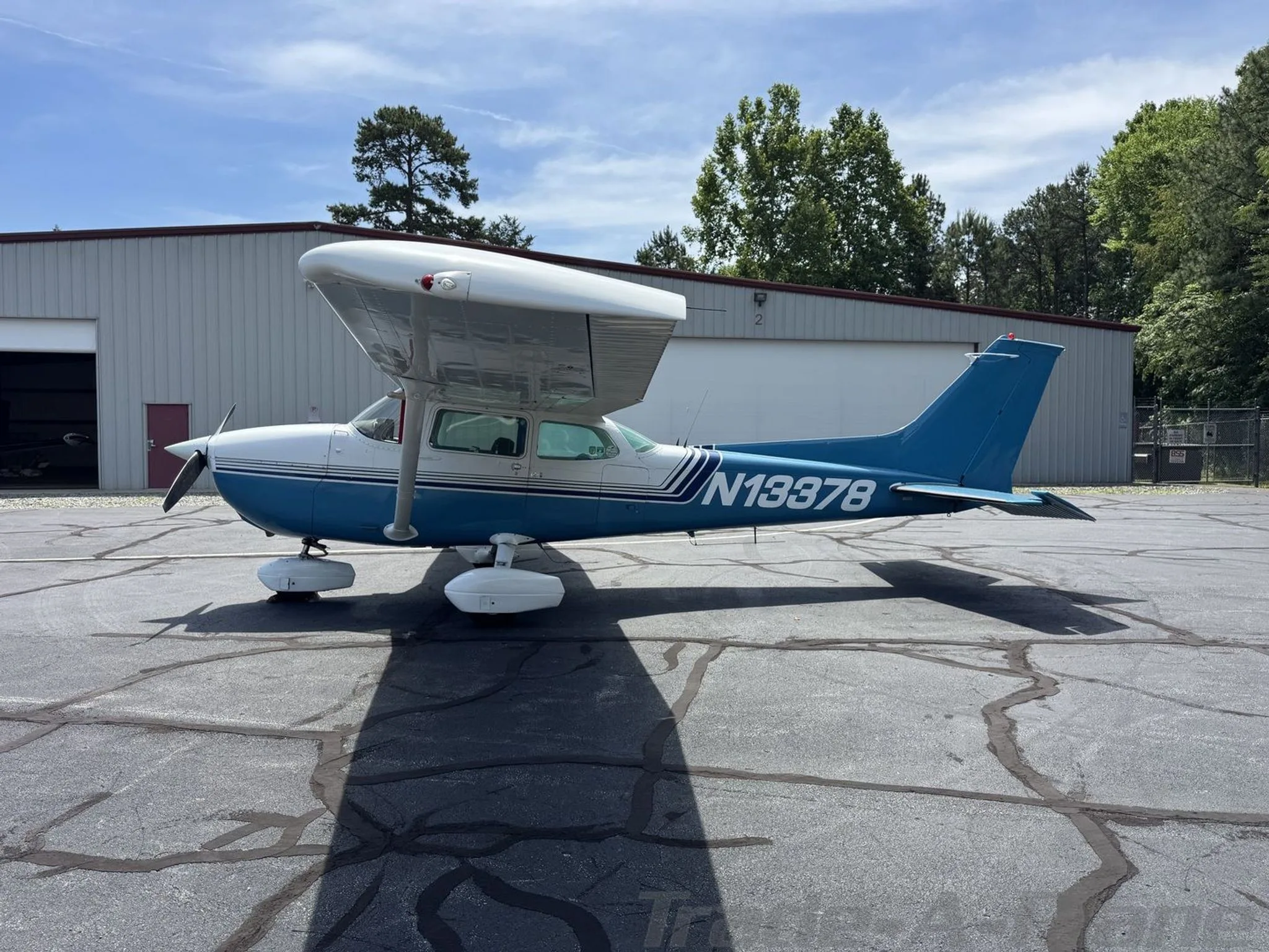 A blue and white Cessna 172 Skyhawk (N13378) parked on an asphalt apron next to a hangar.