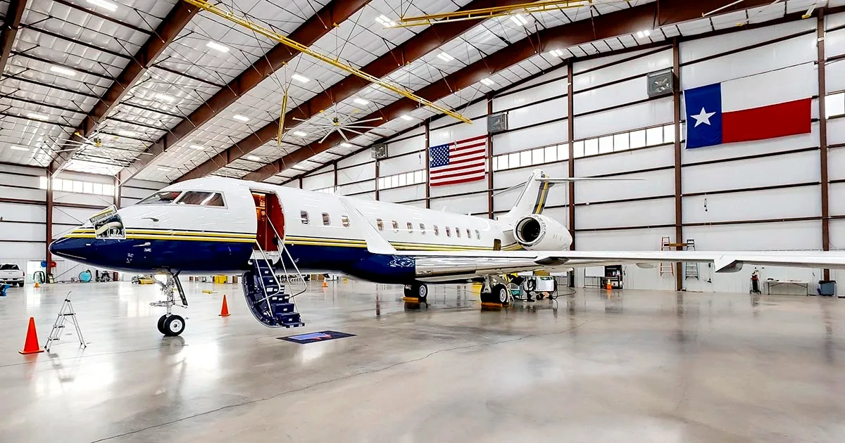 A white business jet with blue and gold livery parked in a hangar, with its main door open and stairs extended.