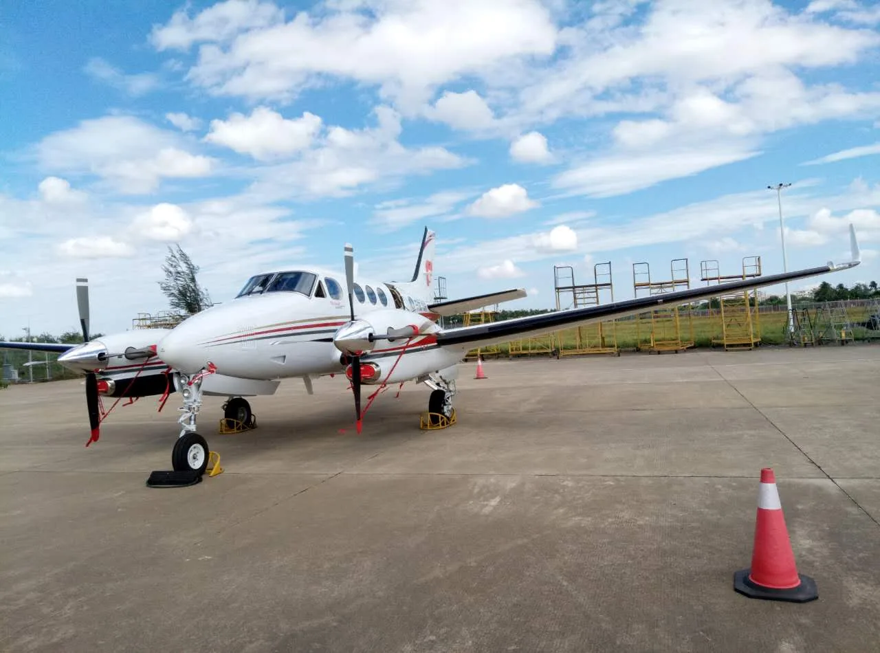 A King Air aircraft is parked on the tarmac with wheel chocks and propeller covers.