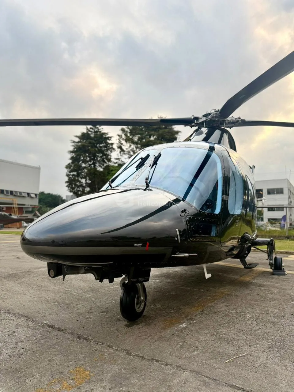 A close-up front view of a black AgustaWestland AW109 helicopter on an apron.