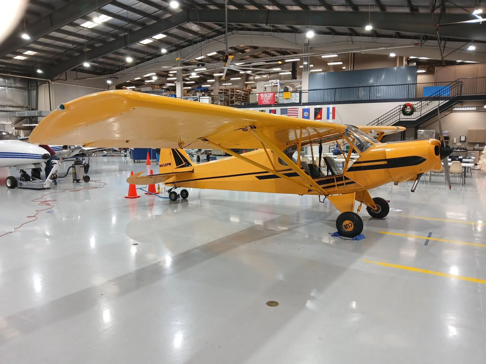 A yellow Piper Cub-style aircraft, N618PM, is parked in a hangar with other aircraft.