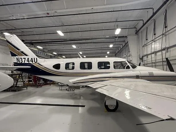 A white and blue twin-engine aircraft with registration N3744U is parked inside a hangar, viewed from the side.