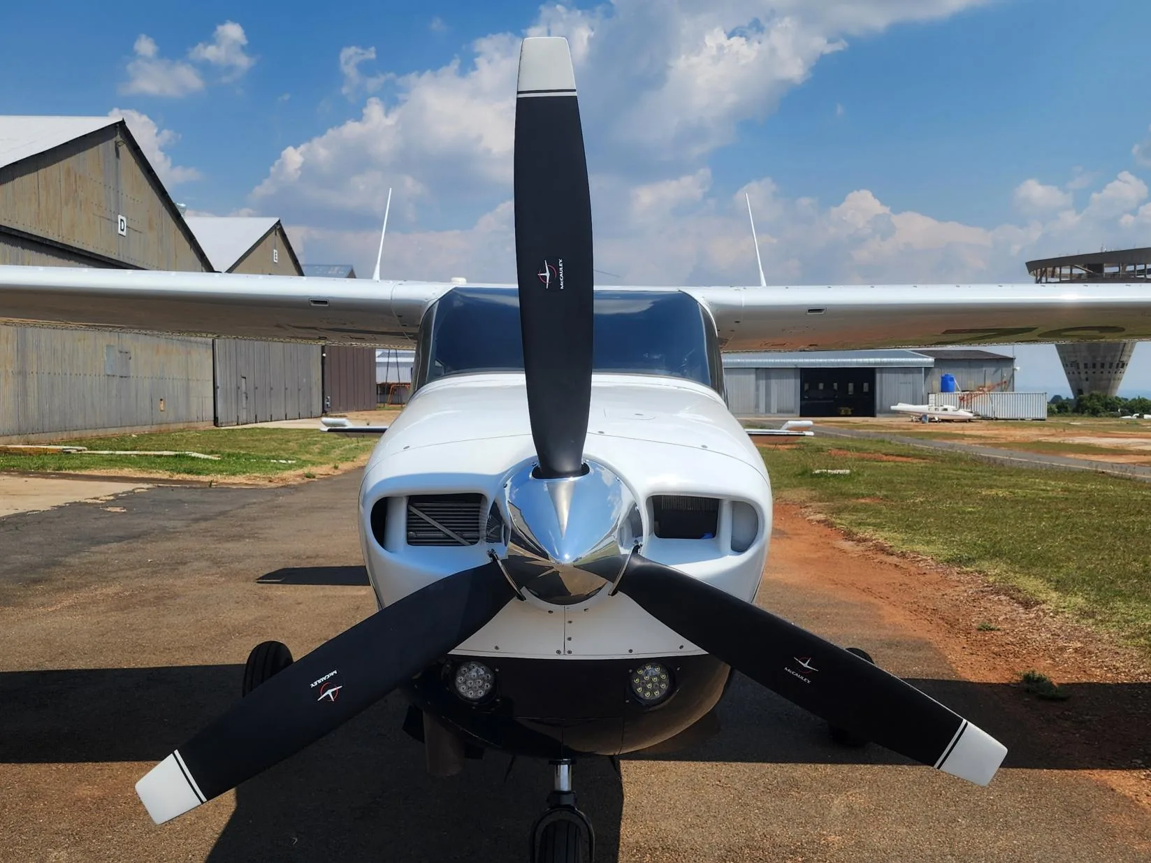 Front view of a white and black single-engine propeller aircraft with a polished spinner, parked on an airfield.