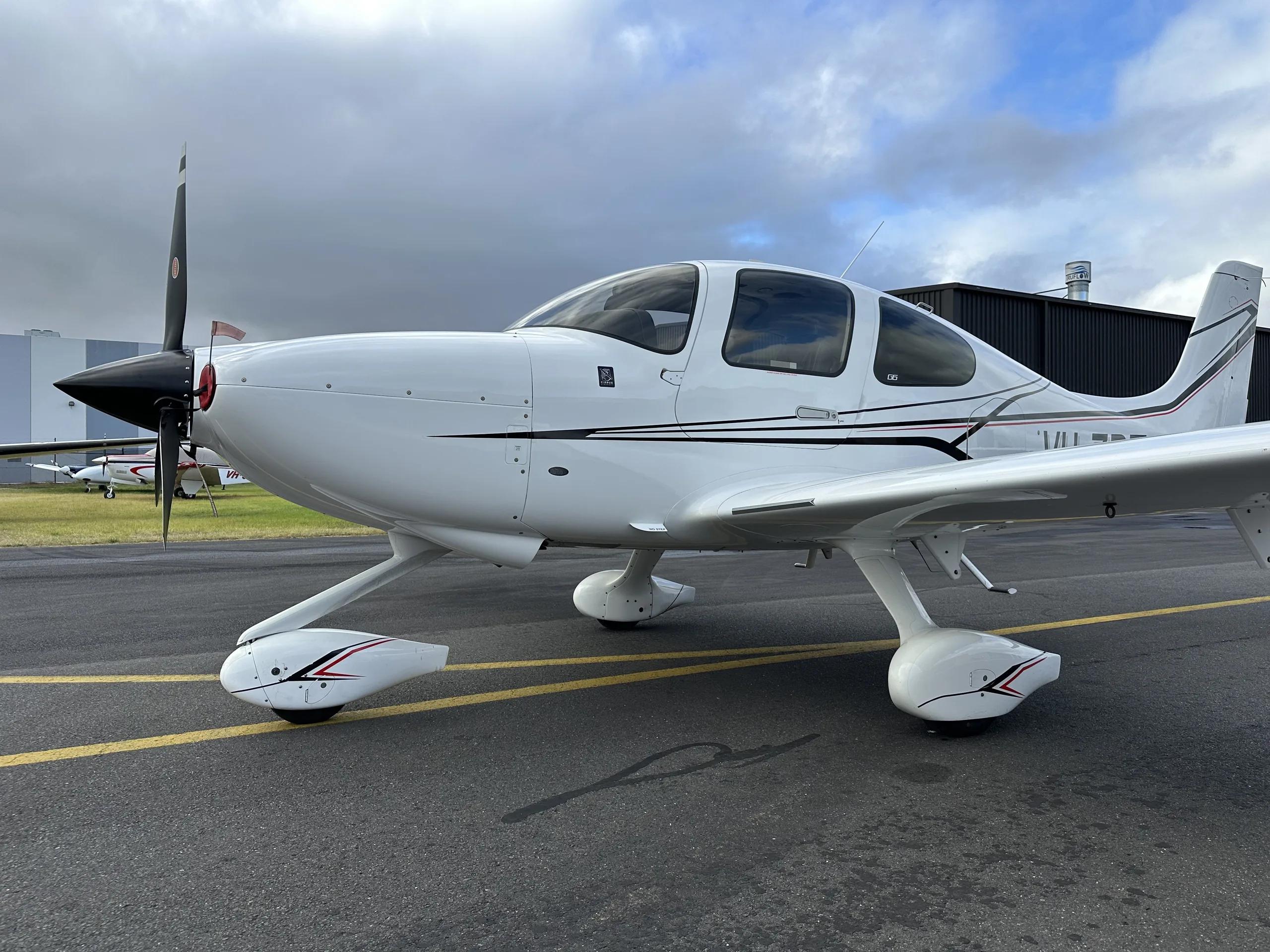 A front-side view of a white Cirrus SR22 aircraft with black and red accents parked on an airfield.