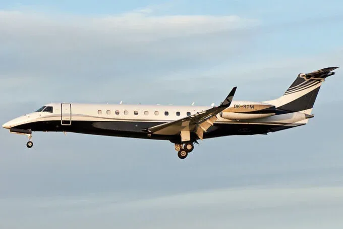 A white and black private jet, registration OK-ROM, in flight with landing gear extended against a light blue sky.