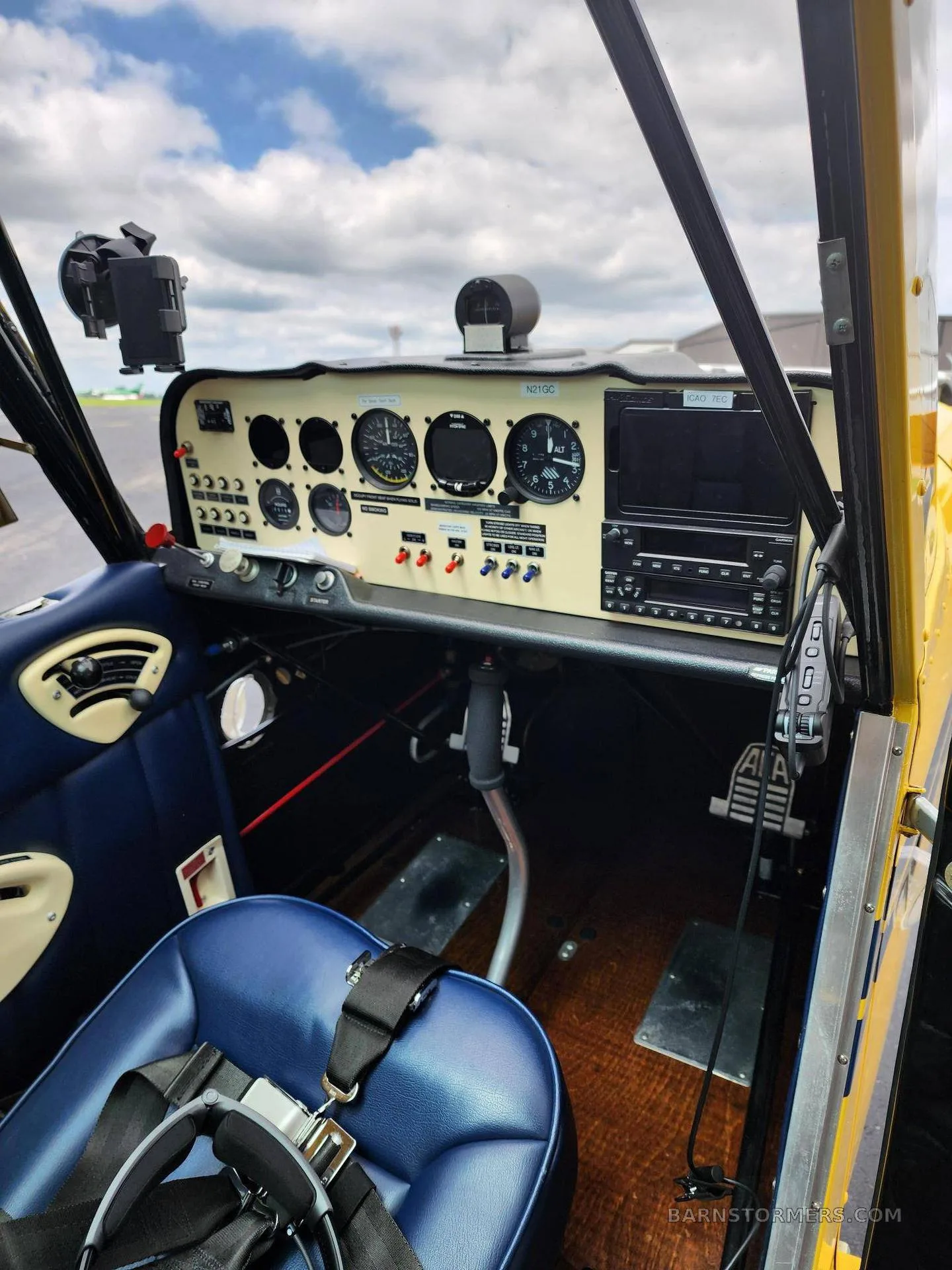 A view of the cockpit of a yellow aircraft with blue seats and a cream-colored instrument panel.