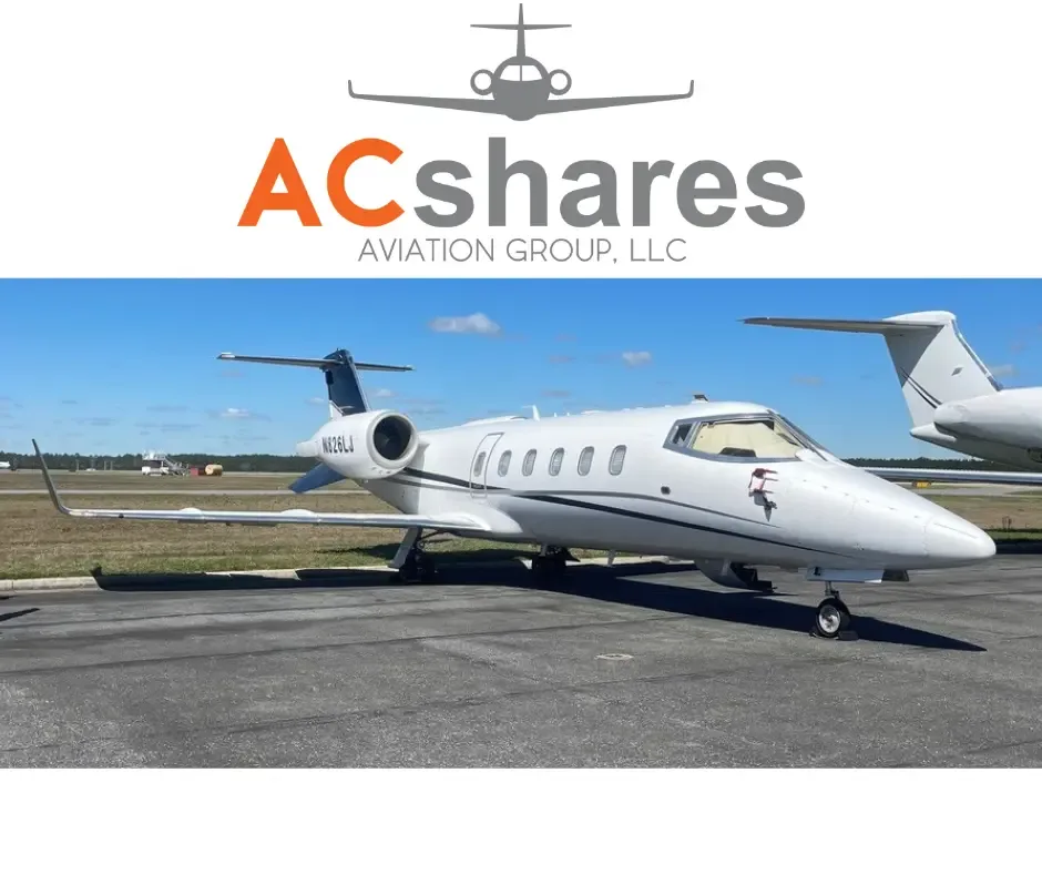 A white Learjet business jet, registration N826LJ, is parked on an airfield under a clear blue sky.