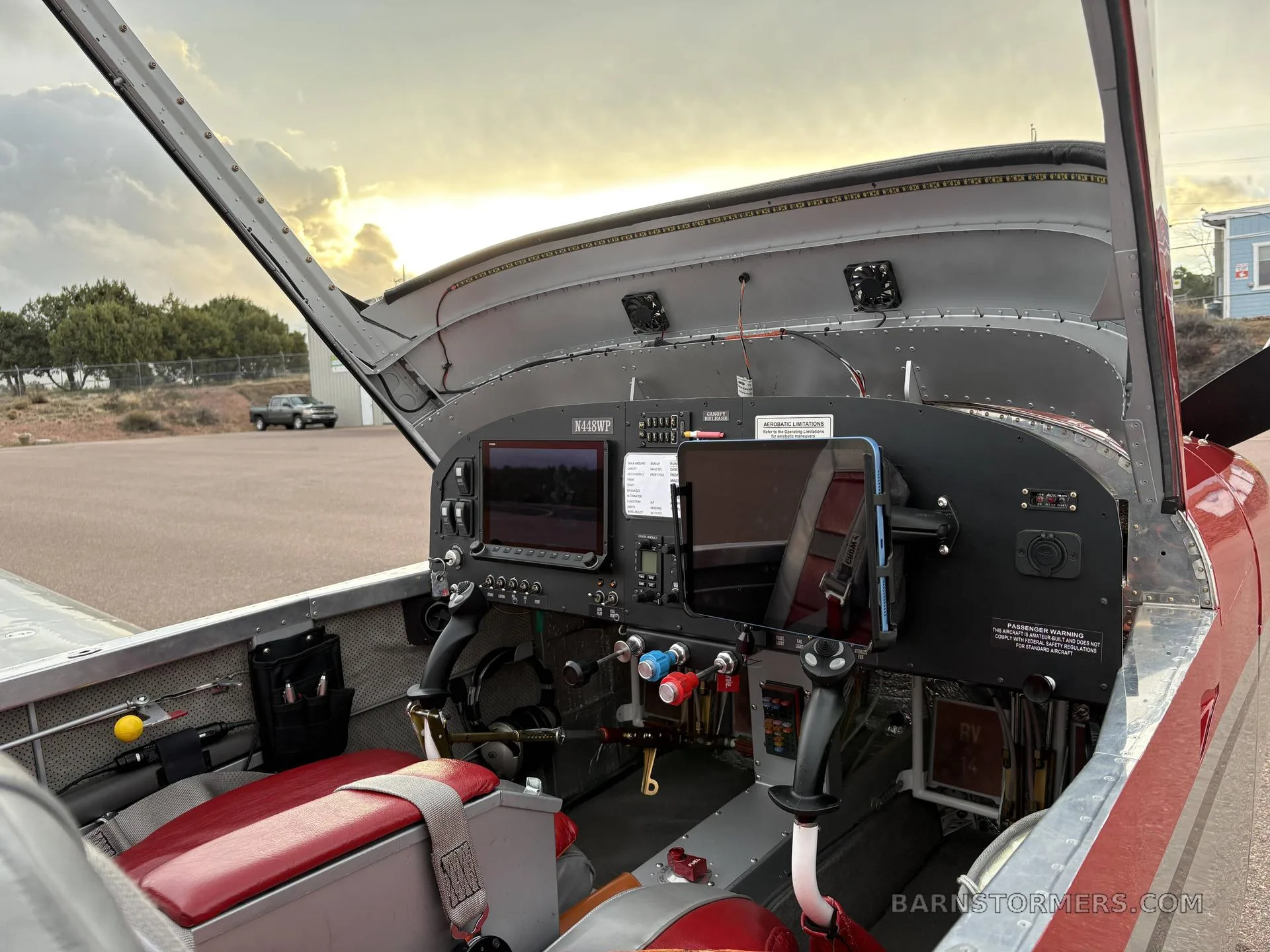 The cockpit of a red and silver aircraft, N448WP, showing the instrument panel with dual screens and red upholstered seats.