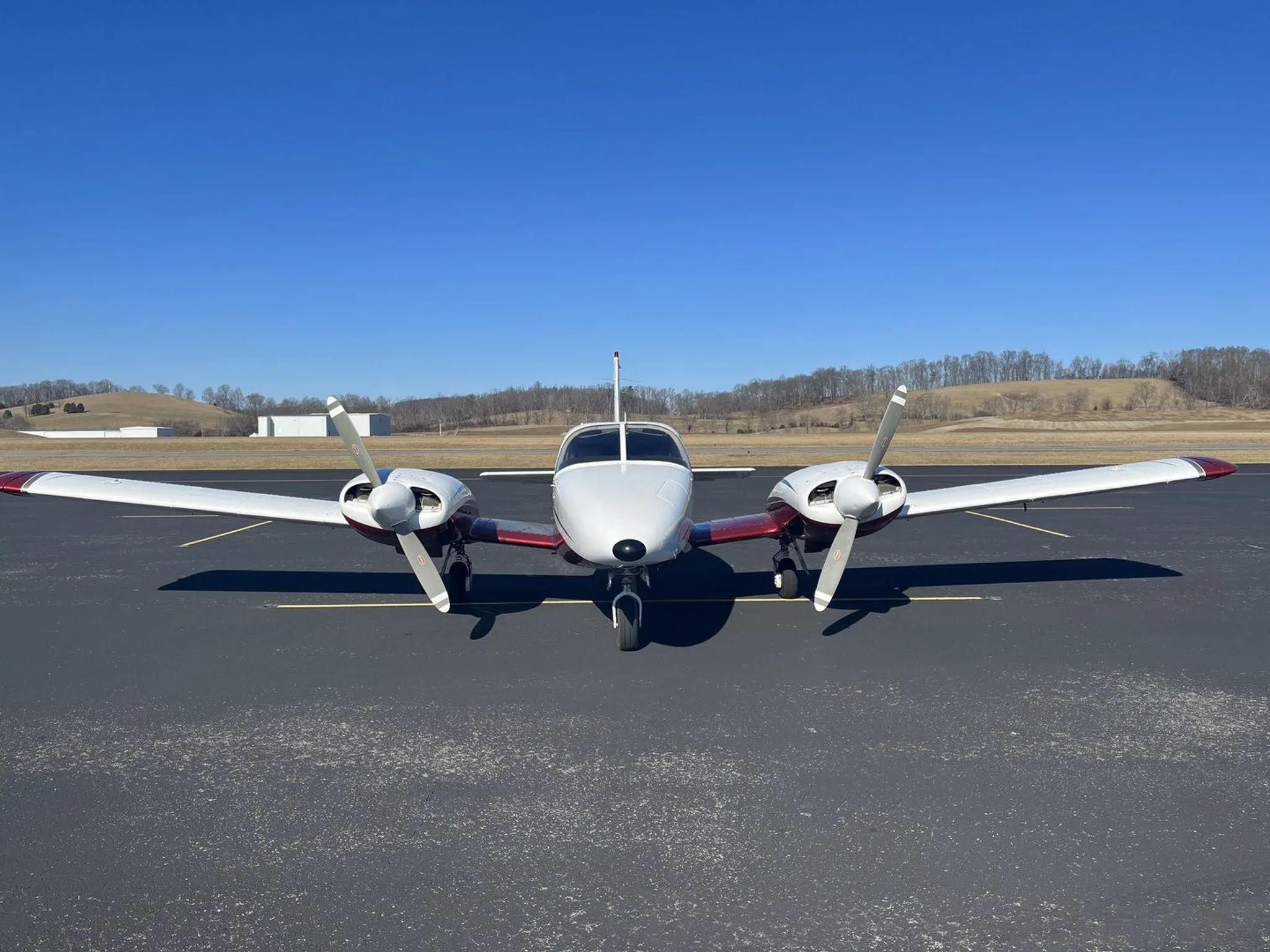 A head-on view of a white and maroon Piper N2618M twin-engine aircraft with both propellers visible, parked on an airfield.