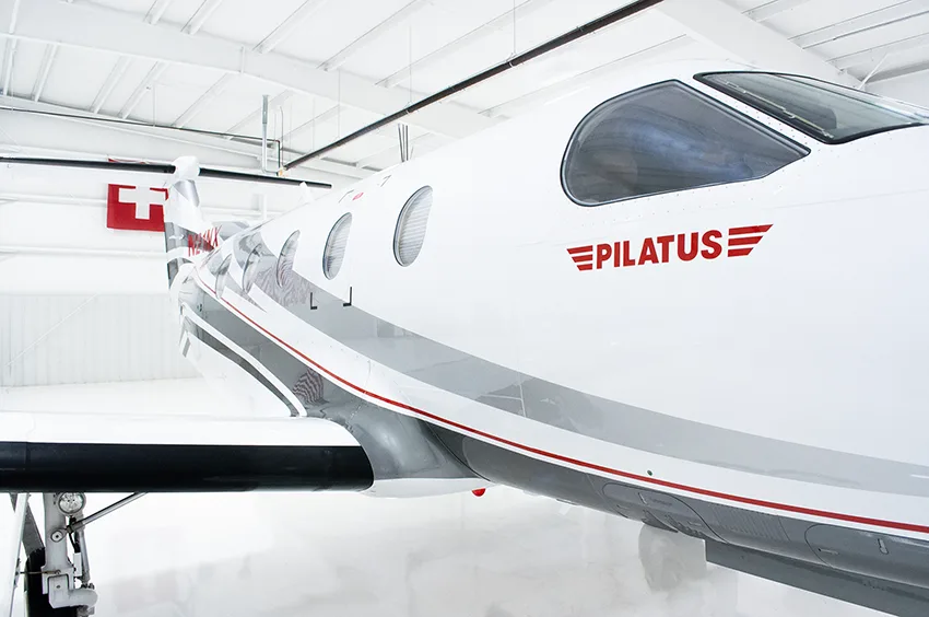A close-up view of the tail and rear fuselage of a white Pilatus PC-12NG aircraft with gray and black stripes and registration N21NX.