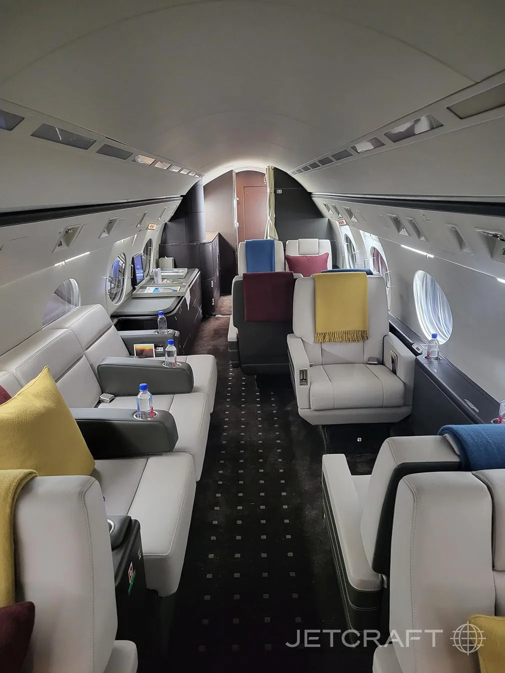 A view of the business jet cabin showing light grey seats, a side divan, and a small table with water bottles.