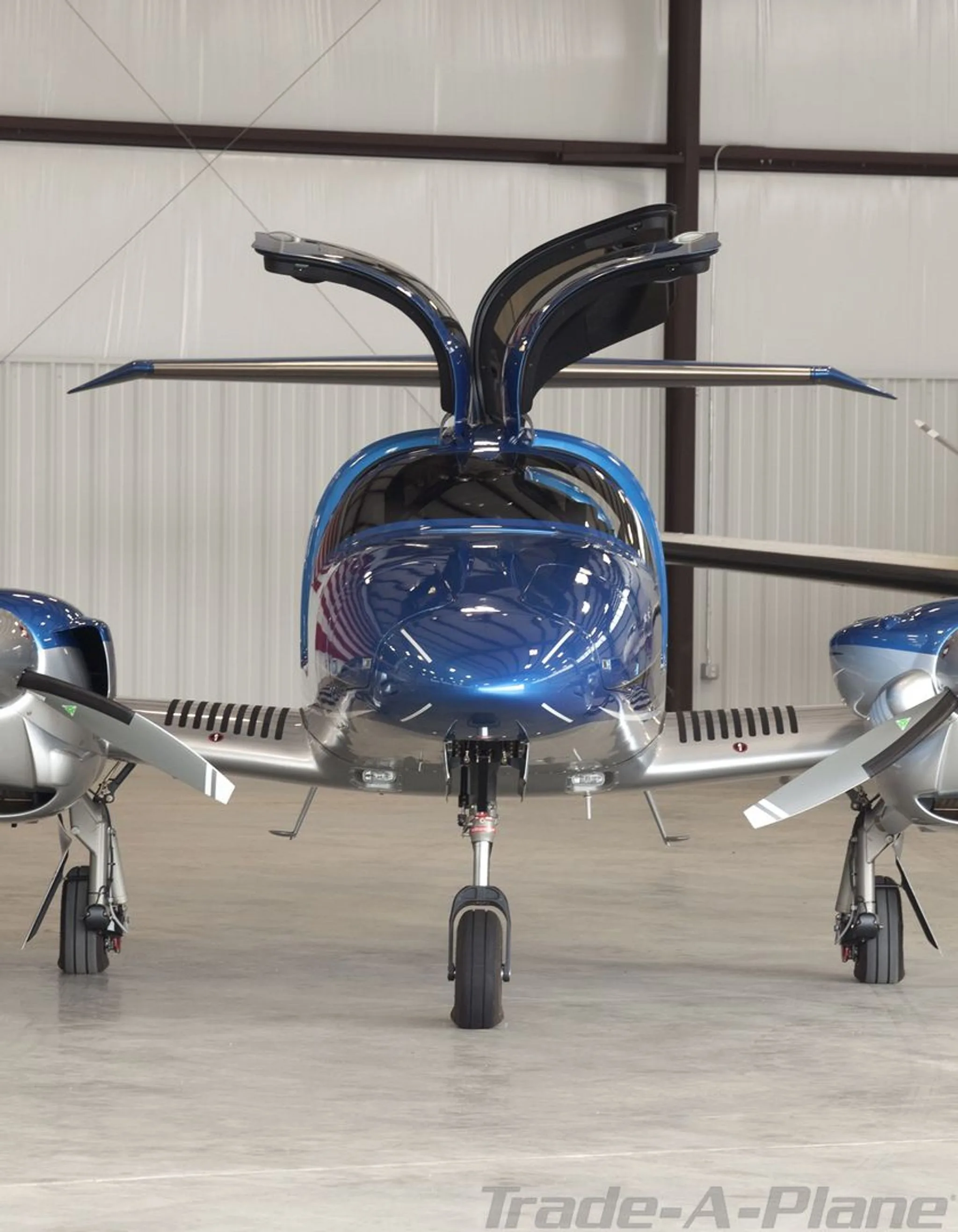 A front view of the blue and silver Diamond DA62 aircraft with its gull-wing doors open, parked in a hangar.