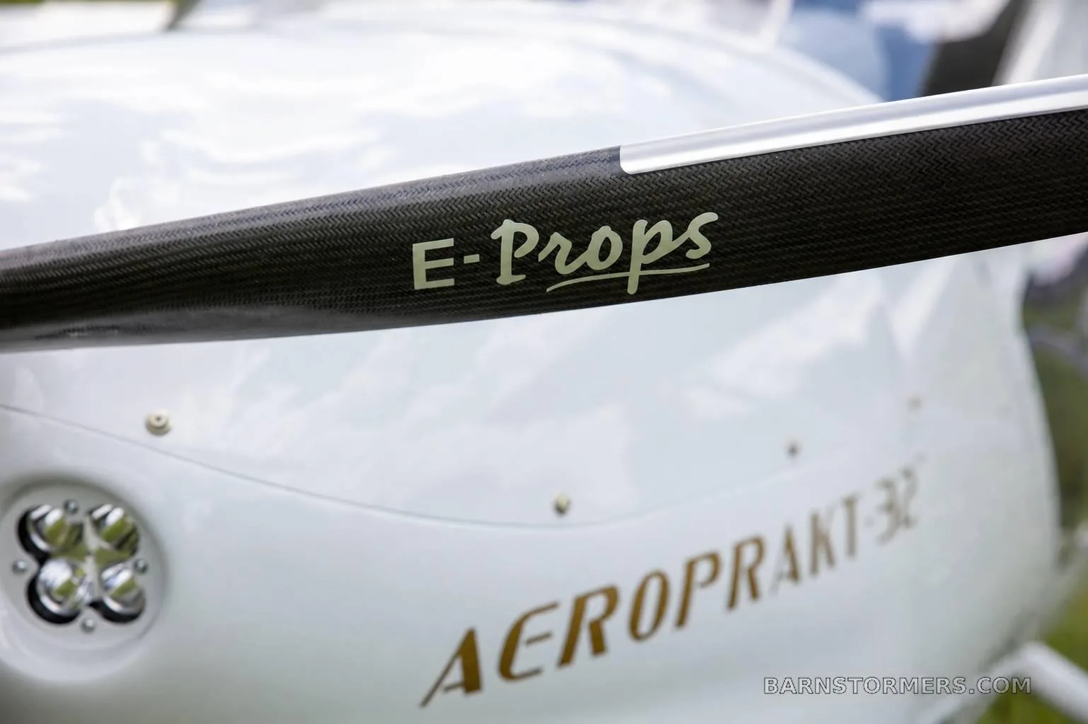 A close-up of the E-Props propeller blade and the 'AEROPRAKT-32' text on the aircraft's white cowling.