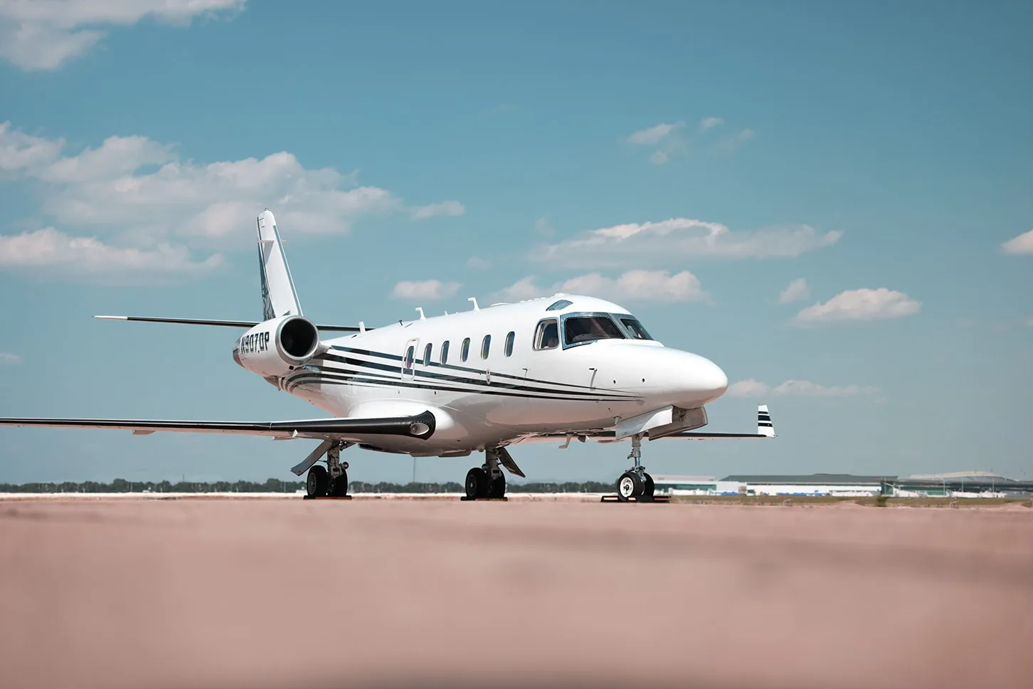 A white business jet with black stripes, registration N907DP, parked on a tarmac under a blue sky.