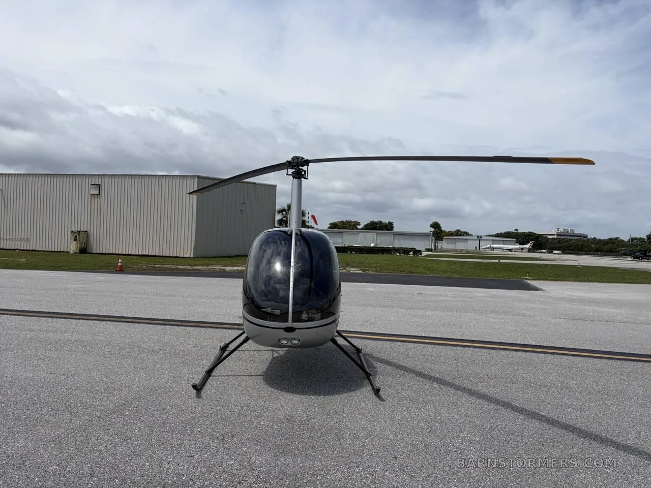 A silver Robinson R22 Beta II helicopter (N674RG) with dark tinted windows, viewed from the front, parked on an asphalt tarmac.