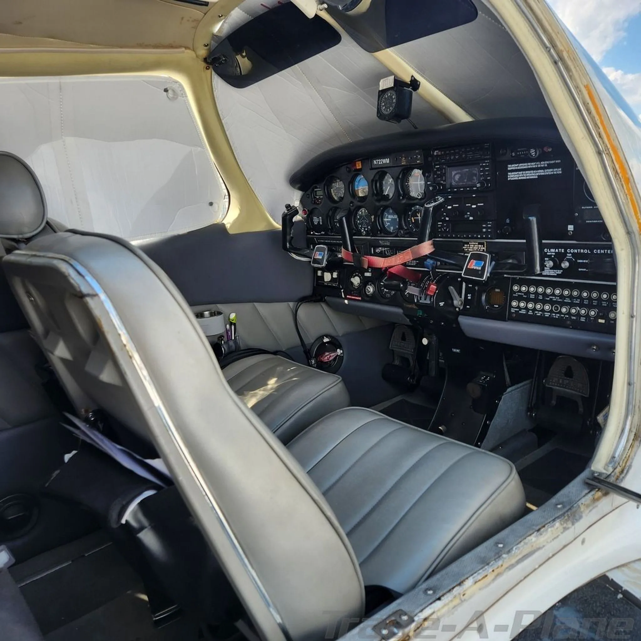 The cockpit of a Piper Cherokee, showing the instrument panel and front grey seats.