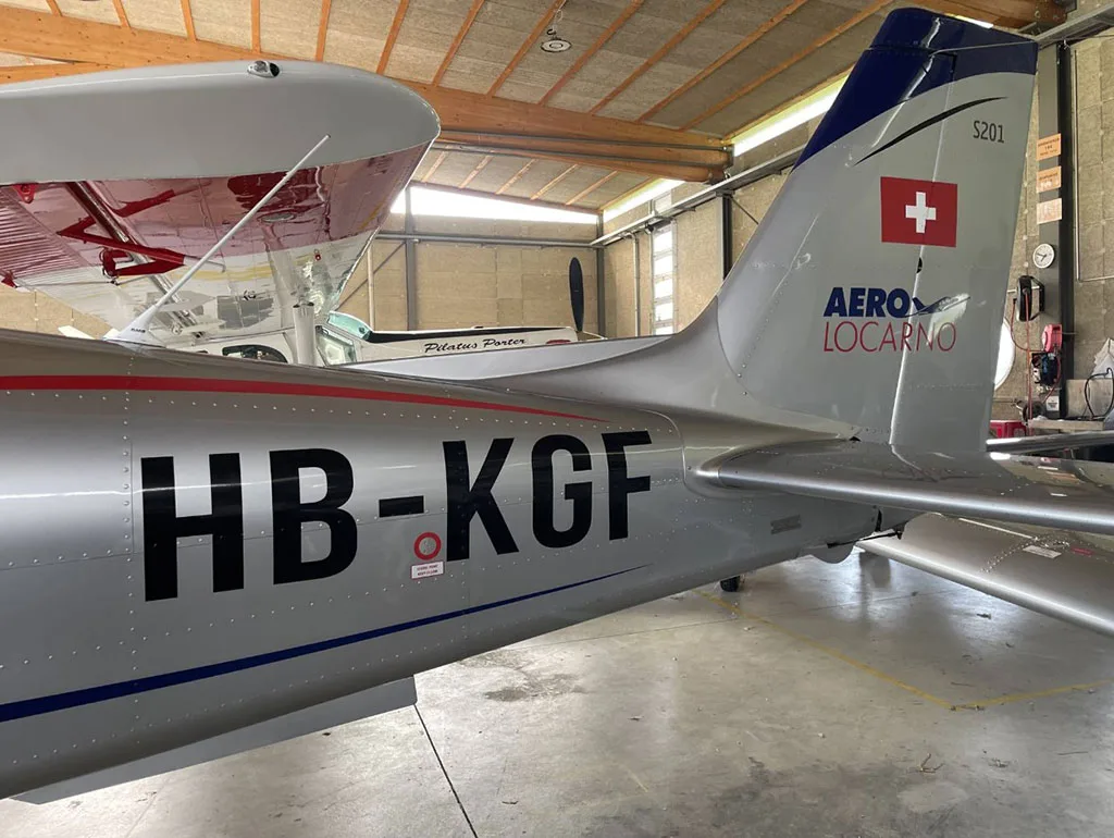Close-up of the tail of a silver Sonaca aircraft with registration HB-KGF, showing the Swiss flag and 'AERO LOCARNO' text.
