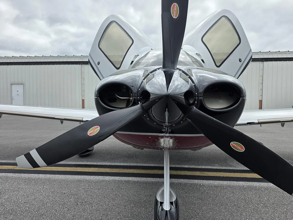 A head-on view of a single-engine aircraft showing its black propeller and open cabin doors.