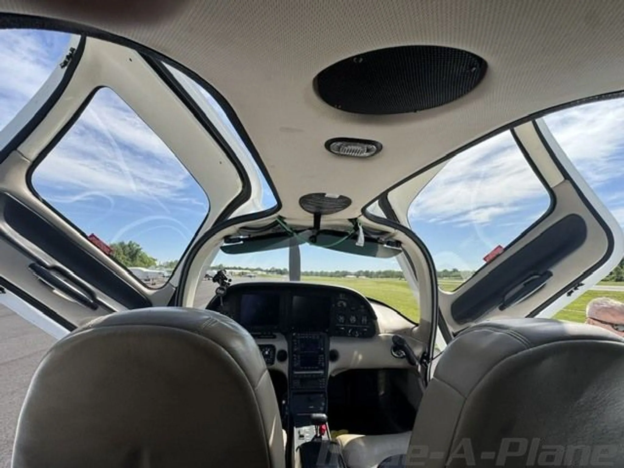 View from inside the cockpit of a Cirrus SR22, looking forward with the doors open to a sunny airfield.