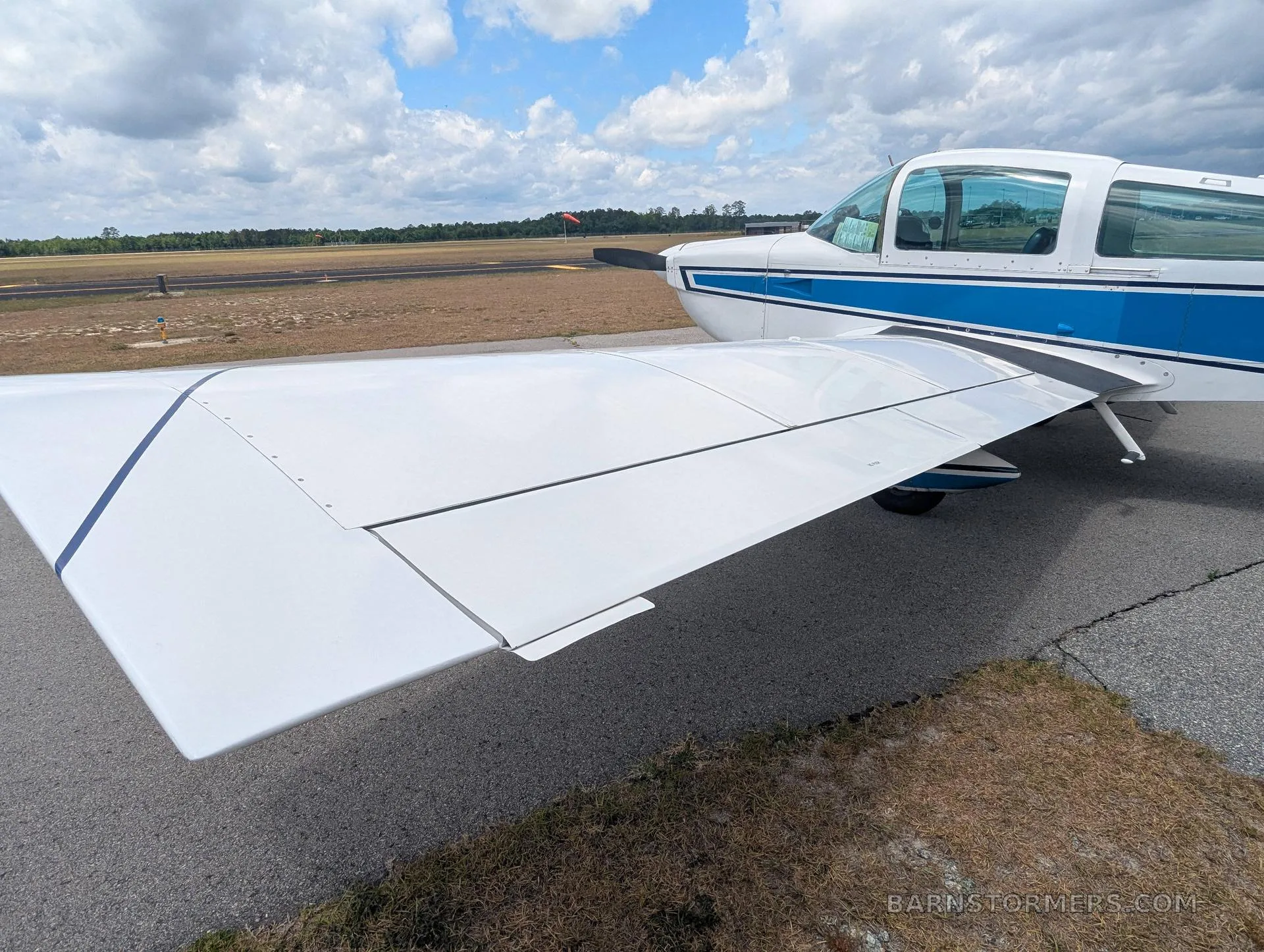 A close-up view of the right wing and front fuselage of a white and blue Grumman AA-5 aircraft with registration N74099 on an airfield.