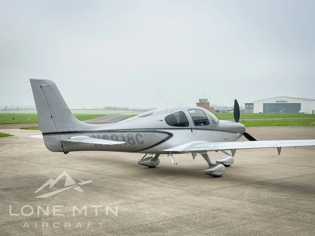 A silver Cirrus SR22 aircraft, registration N6918C, parked on an airfield with a control tower in the distance.