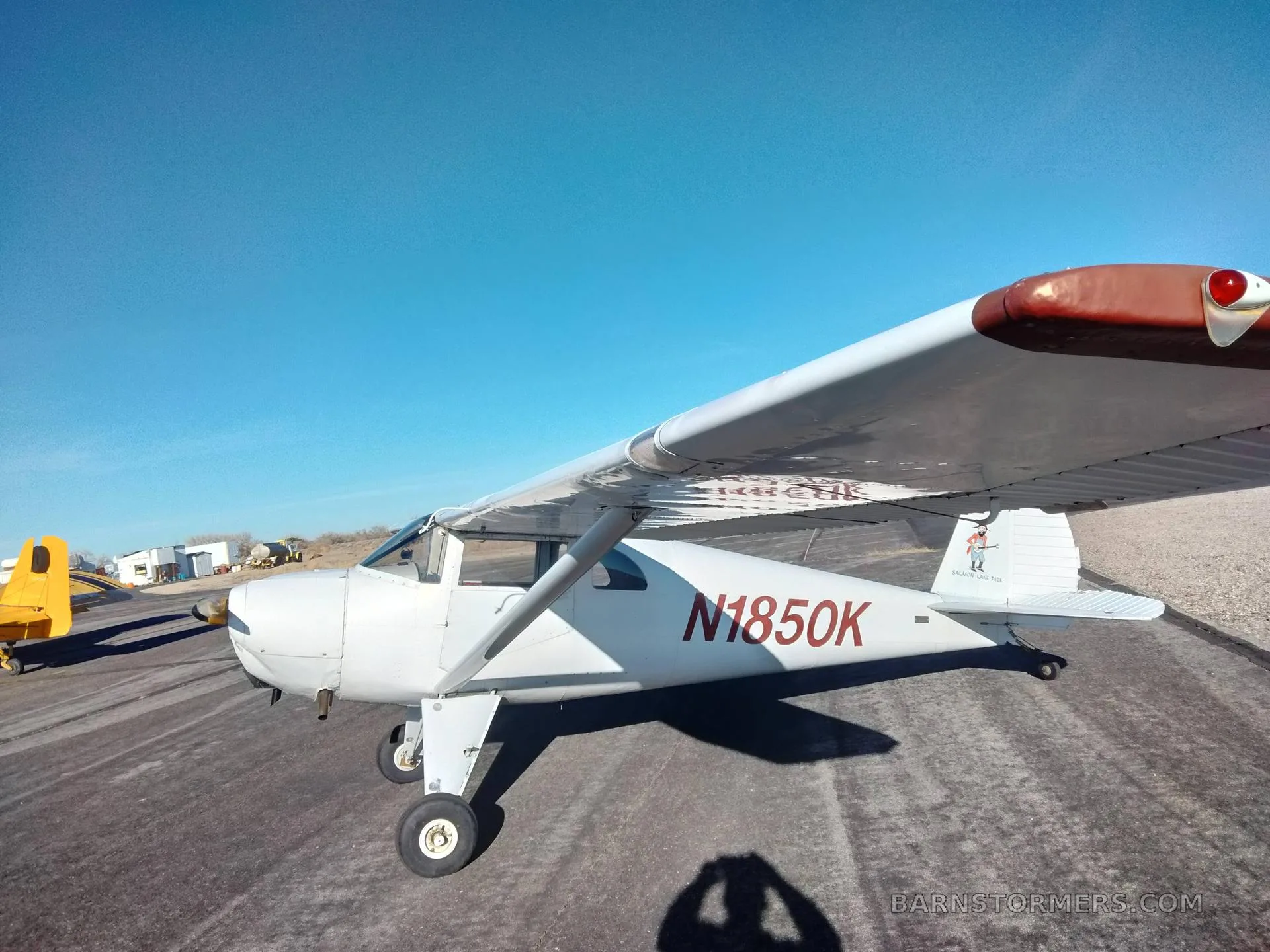 A white Luscombe 8A aircraft with red N1850K registration is parked on an asphalt runway under a clear blue sky.