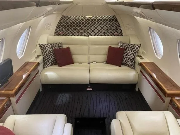 A cream leather sofa with red and patterned pillows is at the rear of the aircraft cabin.
