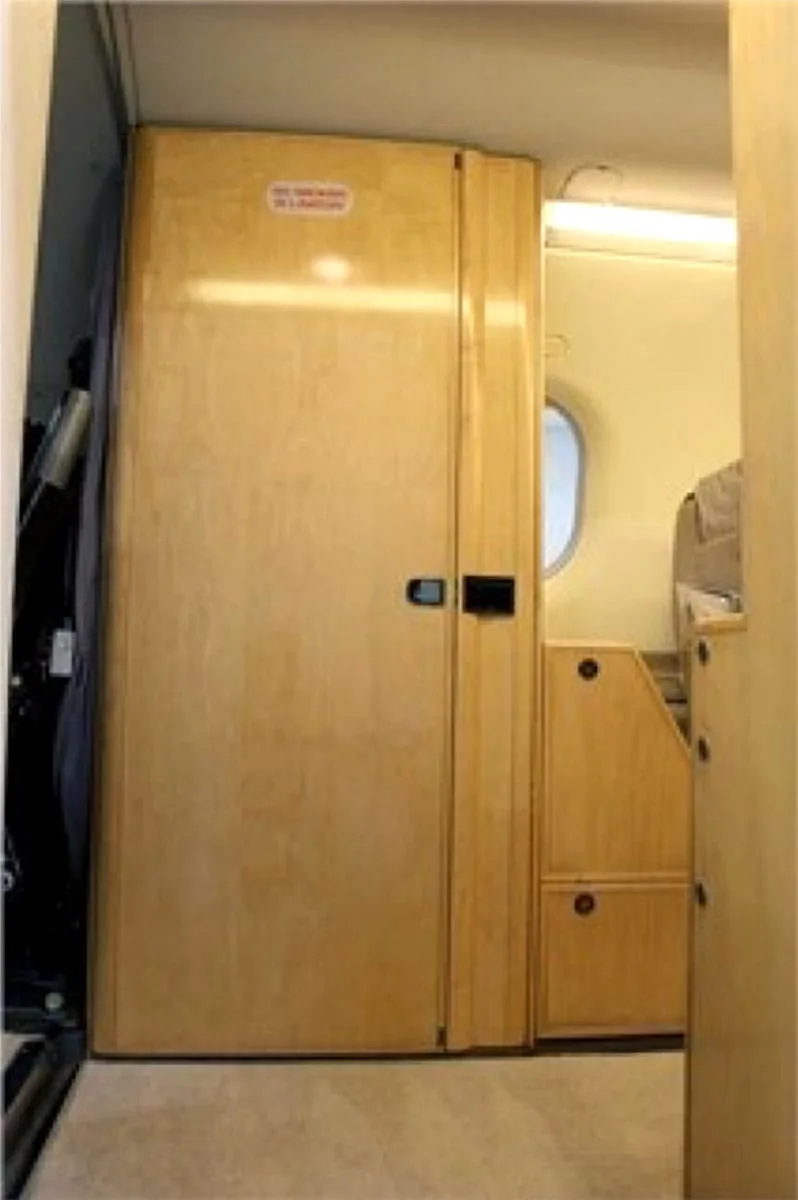 A light wood-paneled door inside an aircraft cabin, with a small storage unit next to it.