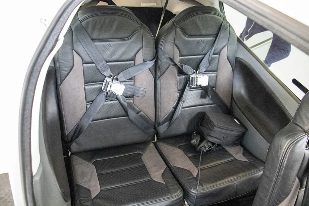 The black leather interior seats of a Cirrus SR22 aircraft, featuring seatbelts and a small bag on one seat.