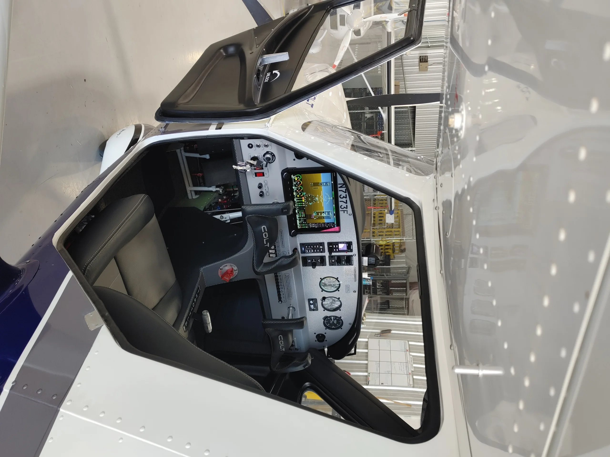 An angled view into the open cockpit of a Texas Aircraft Colt N7373F, showing the instrument panel and controls.