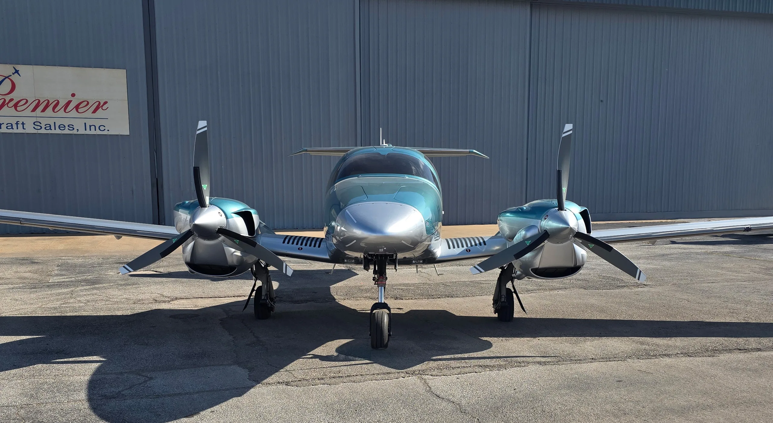A head-on view of a teal and silver Diamond DA62 twin-engine aircraft parked on an asphalt ramp.