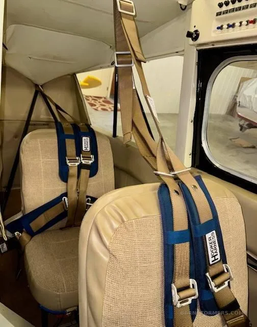 The interior of an aircraft cabin showing two tan seats with blue and tan Hooker Harness seatbelts.