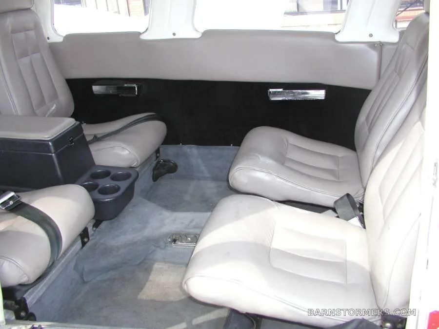 The aircraft's interior cabin showing light gray leather seats, a center console, and gray carpet from a rear perspective.
