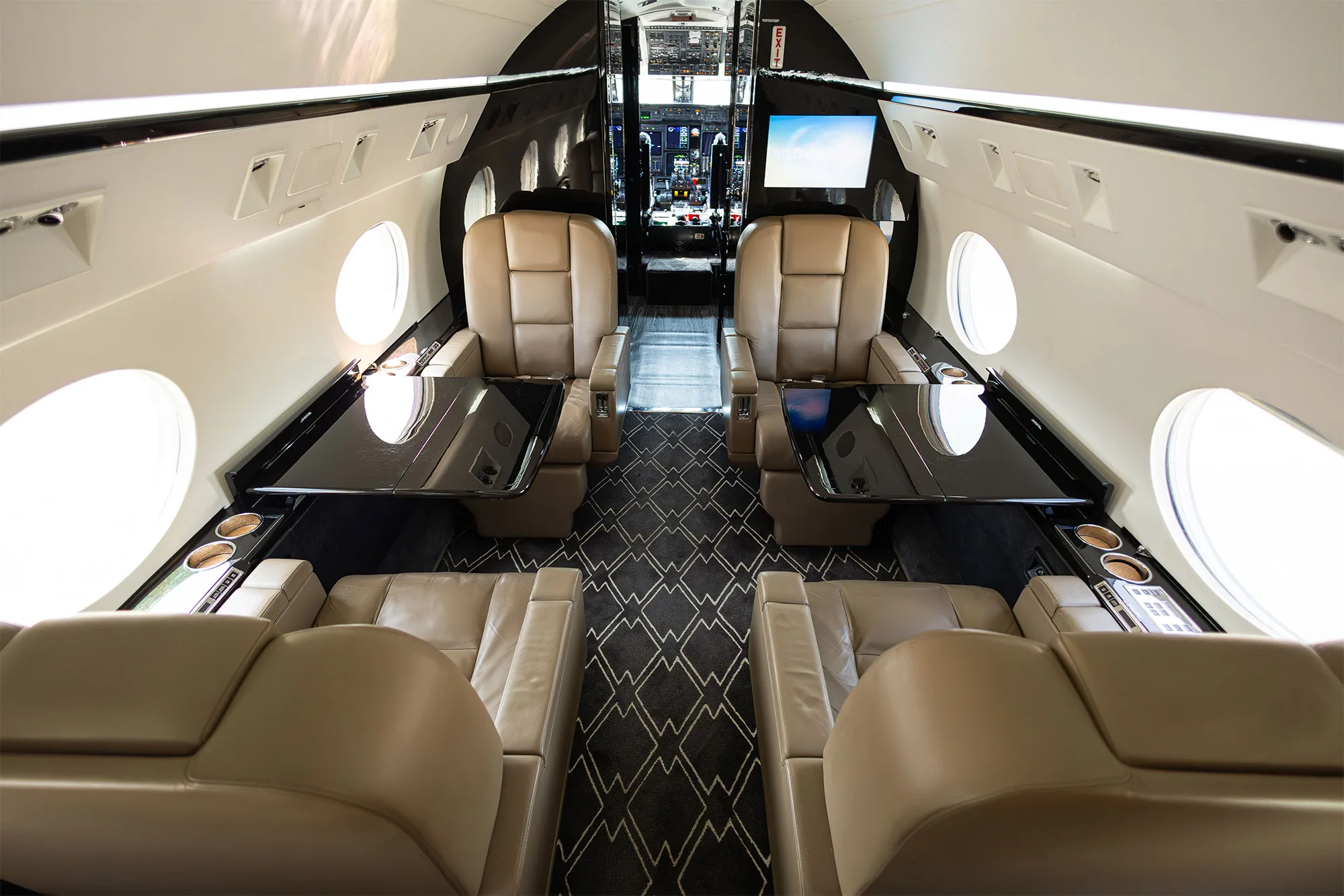 Aircraft cabin interior featuring leather seats and black tables.