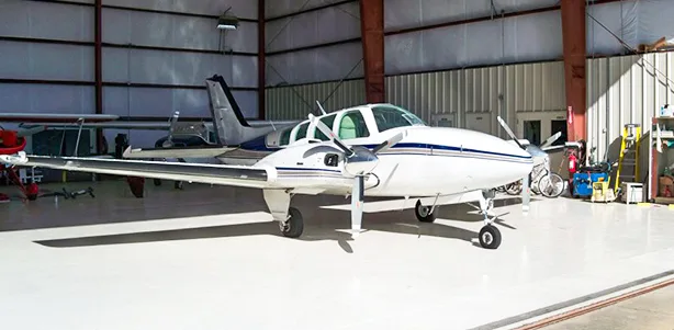A white and blue Beechcraft Baron sits in a hangar.