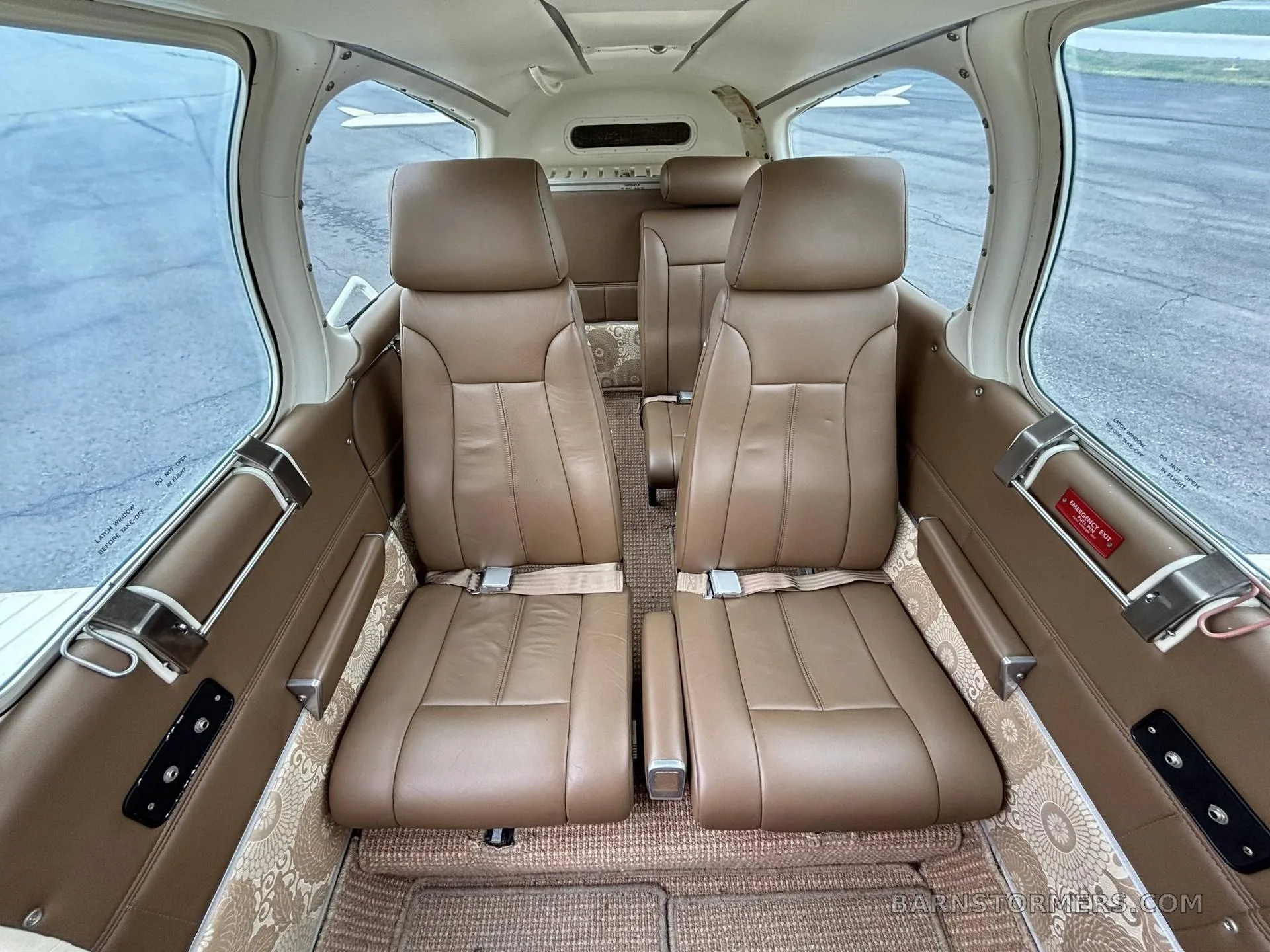 The interior cabin of a small aircraft featuring brown leather seats and patterned carpet.