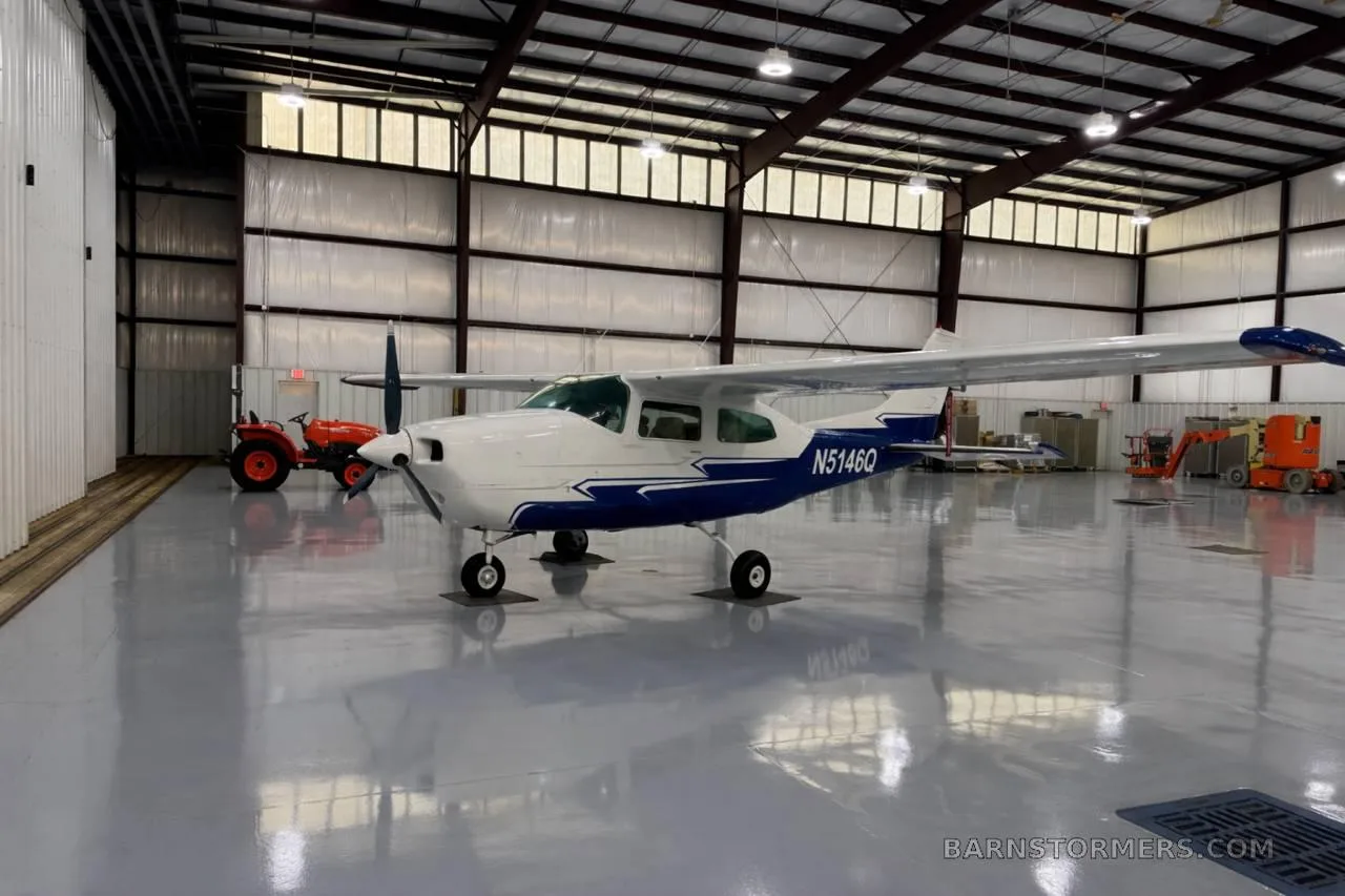A white and blue Cessna 182 (N5146Q) is parked in a brightly lit hangar.